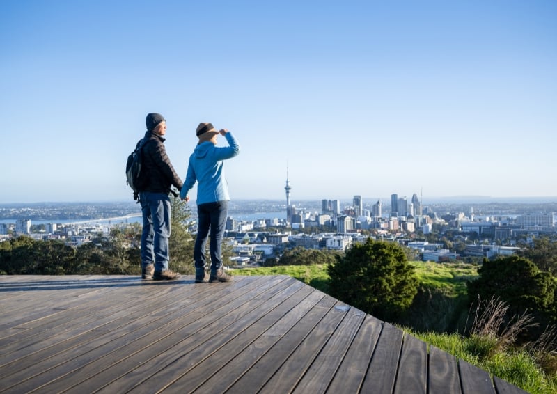 A photo of a couple holding hands as they look out on the city of Auckland, New Zealand.