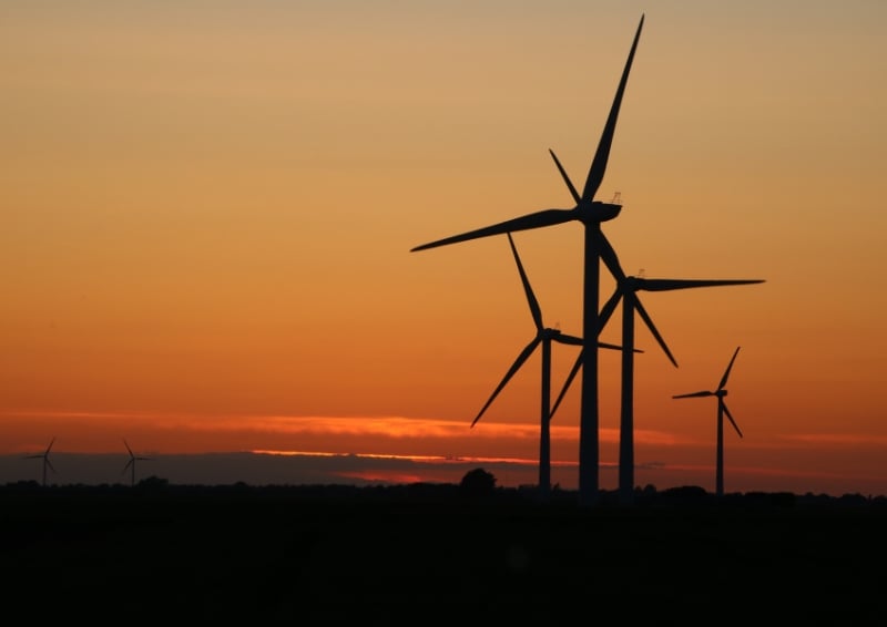Wind turbines at a wind farm silhouetted against an orange sunset sky, generating renewable energy on a rural landscape.