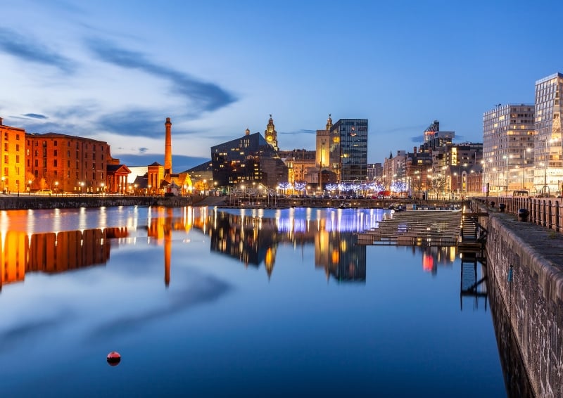 A panoramic picture of the Royal Albert Dock in Liverpool at night, with lights illuminating the buildings.