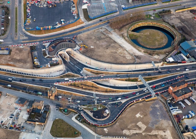 An aerial photograph of the entrance to the Silvertown Tunnel in east London. It's mostly roads with cars travelling on them, but two lead and disappear into the tunnel. 