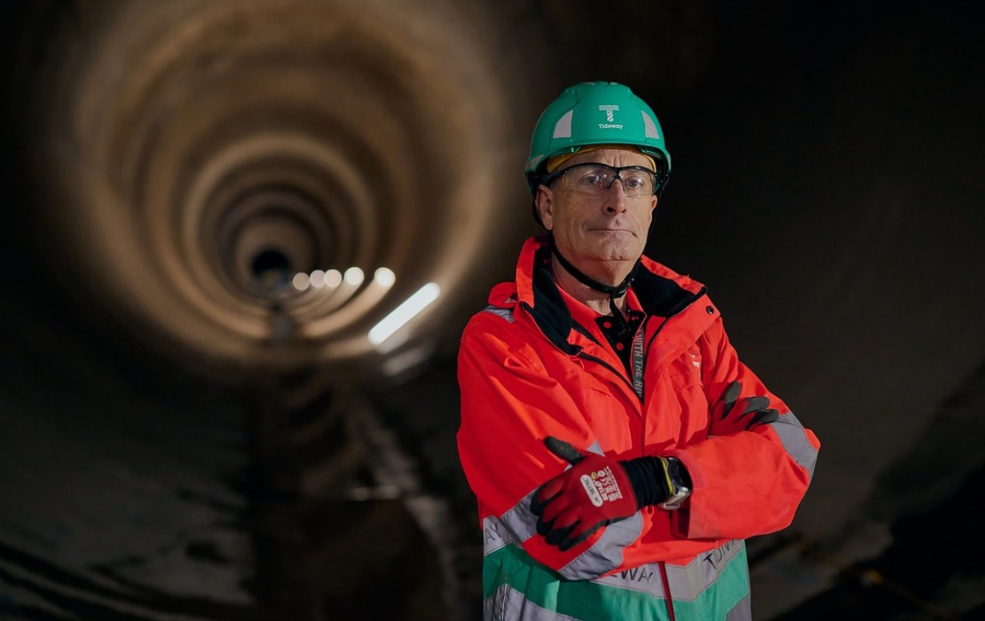Andy Mitchell in high-visibility safety gear and green hard hat standing inside a large tunnel under construction for the Thames Tideway project.