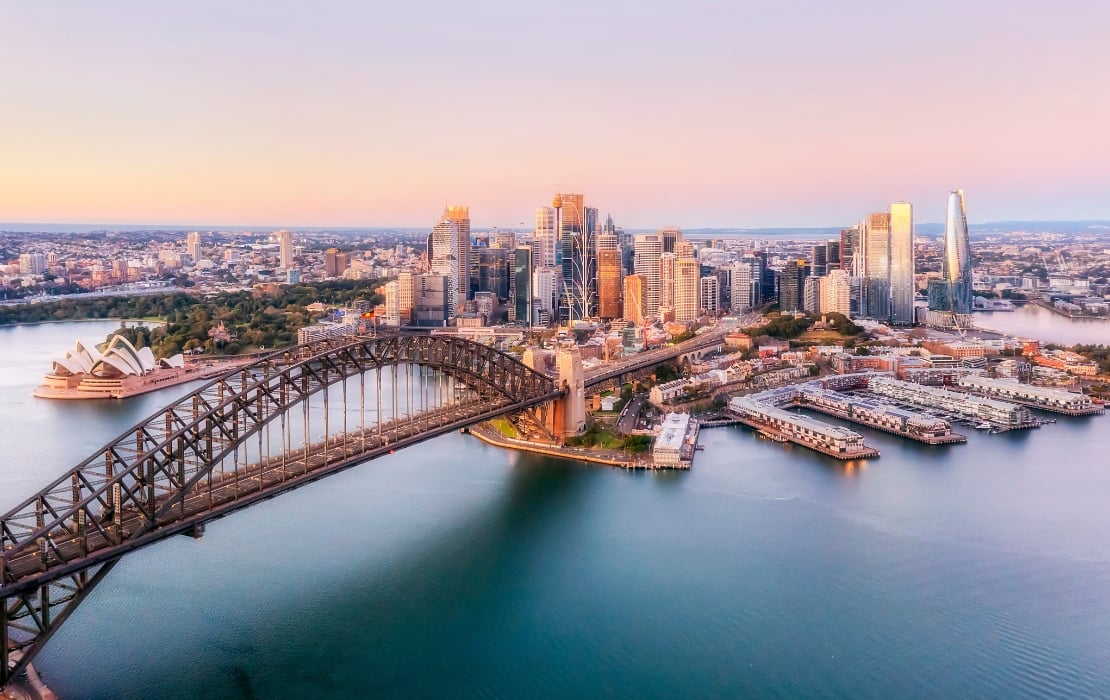 An aerial view of the Sydney Harbour Bridge in Australia in the early hours of the morning. From this angle the city is visible in the background.