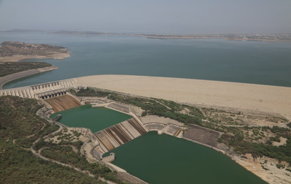 Aerial view of Mangla Dam with large reservoir, spillway gates, and surrounding arid landscape, part of a major hydroelectric and irrigation project.”
