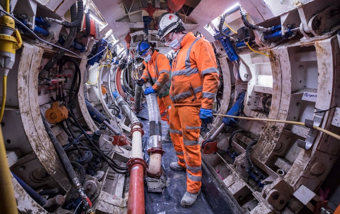 Workers inside a tunnel boring machine during Thames Tideway Tunnel construction, surrounded by hydraulic systems and engineering equipment.
